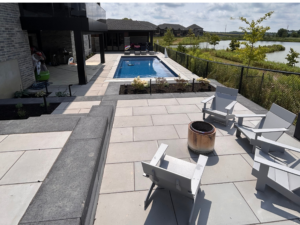 Modern hardscaped backyard featuring large interlocking pavers, a pool, retaining wall, and moveable fire pit.