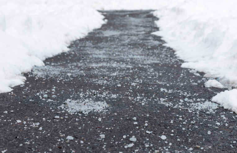 Rock salt sprinkled on a concrete sidewalk for ice prevention in winter.